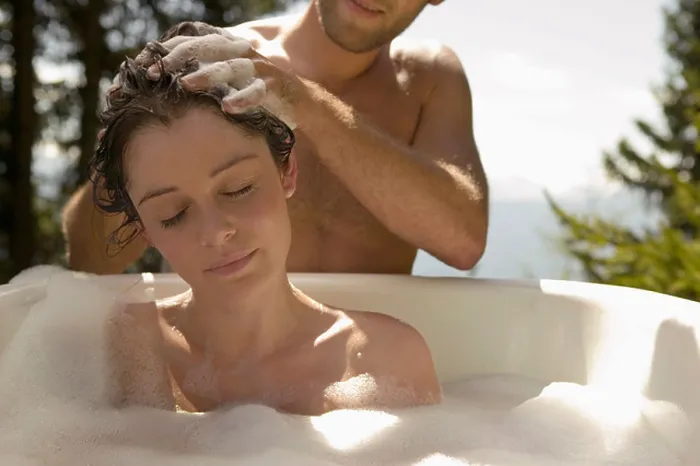 Framed Print : Young woman lying in bathtub, young man washing hair Framed Print : Young woman lying in bathtub, young man washing hair