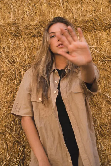 Framed Print : Young woman standing in front of hay bales making rejecting hand gesture, portrait Framed Print : Young woman standing in front of hay bales making rejecting hand gesture, portrait