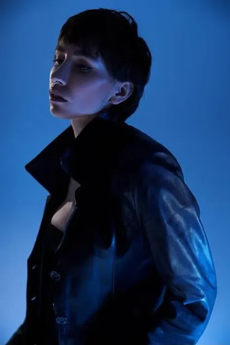 Framed Print : Young woman striking a pose in a black leather jacket against a vibrant blue backdrop Framed Print : Young woman striking a pose in a black leather jacket against a vibrant blue backdrop