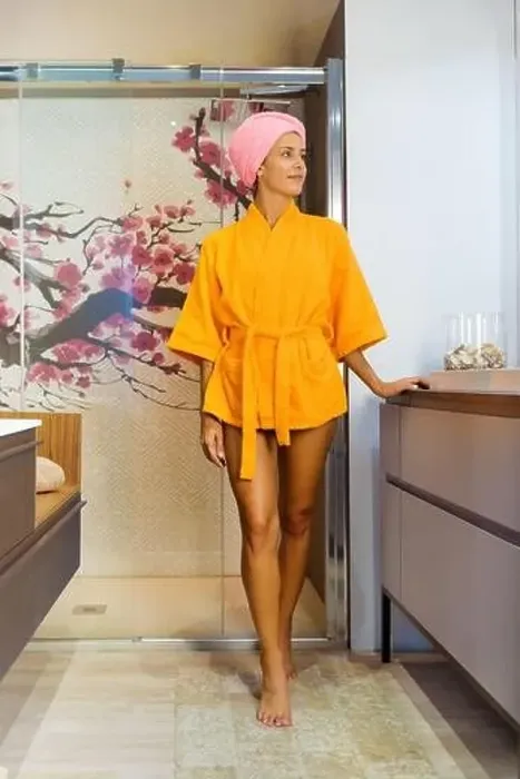 Framed Print : Young woman wearing a colorful orange bathrobe with her hair wrapped in a towel exiting a glass shower cubicle looking