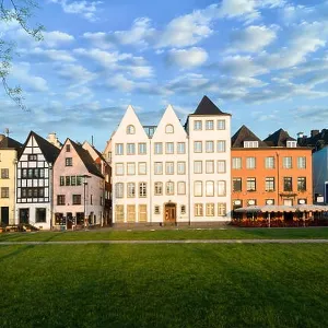 Houses and park in Cologne, Germany. Many of them are colourful, they are facing a public park with green grass and some trees. There is a Cologne bel Houses and park in Cologne, Germany. Many of them are colourful, they are facing a public park with green grass and some trees. There is a Cologne bel