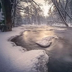 Scenic winter landscape with flowing river and morning light in Finland. Snowy trees