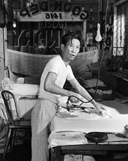 Mature Prints: 1920s CHINESE LAUNDRY MAN LOOKING AT CAMERA IRONING CLOTHES ON BOARD