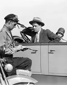Occupations Prints: 1920s MOTORCYCLE POLICEMAN WRITING A SPEEDING TICKET TO A COUPLE SITTING IN CONVERTIBLE SEDAN