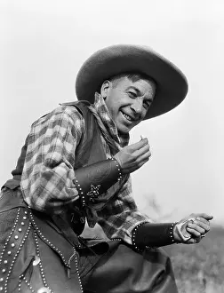 Occupations Prints: 1920s SMILING MAN IN COWBOY HAT VEST CUFFS AND CHAPS ROLLING CIGARETTE