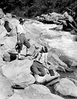 Sisters Prints: 1920s TWO WOMEN SISTERS ON ROCKS BY CREEK TALKING HOLDING FOLDING CAMERA