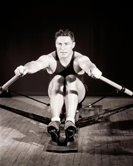 Healthiness Prints: 1930s MAN MUSCULAR ATHLETE CONCENTRATED FOCUSED FACIAL EXPRESSION EXERCISING WORKING OUT ON GYMNASIUM STATIONARY ROWING
