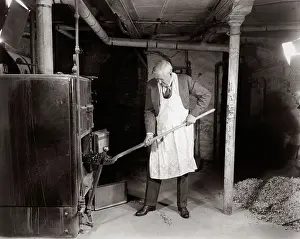 Basement Prints: 1940s ELDERLY MAN IN BASEMENT WEARING APRON SHOVELING COAL INTO FURNACE