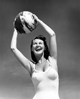 Hars Prints: 1940s SMILING WOMAN IN WHITE BATHING SUIT HOLDING A BEACH BALL OVER HER HEAD OUTDOOR