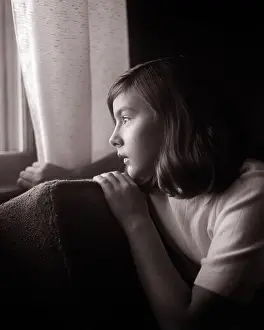 Old Fashion Prints: 1960s SERIOUS SAD TEENAGE GIRL SITTING IN DARKENED ROOM HOLDING BACK CURTAIN LOOKING OUT OF THE WINDOW WITH