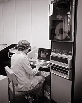Old Fashion Prints: 1970s BACK VIEW OF WOMAN SITTING WORKING AT COMPUTER WORKSTATION NEXT TO A REEL TO REEL STORAGE COLUMN - o4229 HAR001
