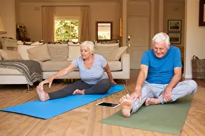 Senior Citizen Prints: Active senior couple stretching while doing yoga together at home