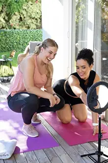 Curly Hair Prints: Adjusting ring light, Diverse female friends crouching on yoga mats on deck in backyard