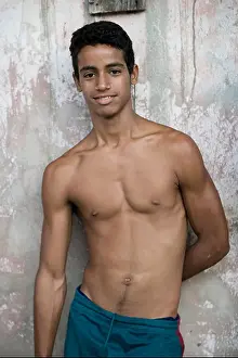 Guantanamo Prints: An adolescent Cuban guy leans against a pastel colored wall in Baracoa