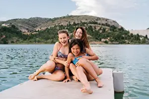 Tickle Prints: Adult Woman in swimwear tickling cheerful children while sitting relaxing on pier embracing each other during summer
