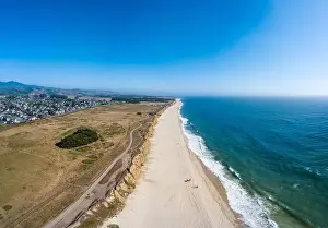Aerial Beach Prints: Aerial Of beach blue waves clashing on the shore on a afternoon with city and mountains hazy horizon