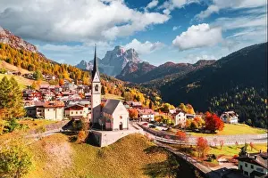 Aerial drone flight over San Lorenzo Catholic church in Selva di Cadore village. Biautiful small city in autumn Dolomites mountains