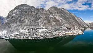 Northern Limestone Alps Prints: Aerial drone shot of Halstatt village at foot of snowy mountain under blue sky in winter time in austria