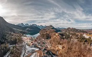 Aerial drone shot of Hohenschwangau by lake in Fussen with view of Alps snow mountain range in Germany winter