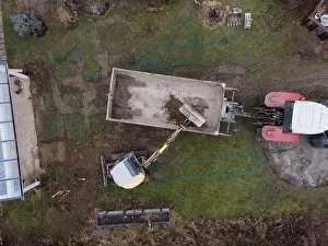 Mover Prints: aerial drone shot of small, yellow excavator stands in a large garden and digs a hole for a pool in austria