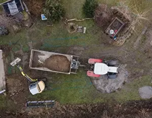 Mover Prints: aerial drone shot of small, yellow excavator stands in a large garden and digs a hole for a pool in austria