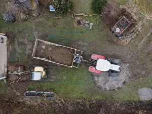 Mover Prints: aerial drone shot of small, yellow excavator stands in a large garden and digs a hole for a pool in austria