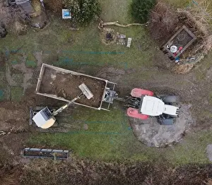 Mover Prints: aerial drone shot of small, yellow excavator stands in a large garden and digs a hole for a pool in austria
