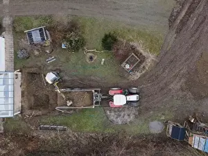 Mover Prints: aerial drone shot of small, yellow excavator stands in a large garden and digs a hole for a pool in austria