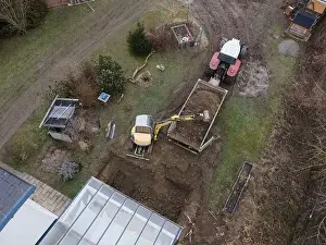 Mover Prints: aerial drone shot of small, yellow excavator stands in a large garden and digs a hole for a pool in austria