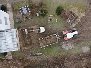 Mover Prints: aerial drone shot of small, yellow excavator stands in a large garden and digs a hole for a pool in austria
