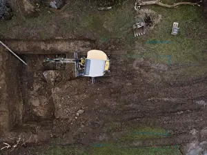Mover Prints: aerial drone shot of small, yellow excavator stands in a large garden and digs a hole for a pool in austria
