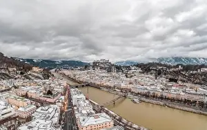 Salzach Prints: Aerial drone shot view of snowy Salzburg city old town by river at dusk with clouds in witner with heavy clouds