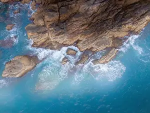 Aerial drone top view of beautiful waves crashing on the rocky island coast