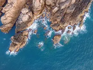 Aerial drone top view of beautiful waves crashing on the rocky island coast