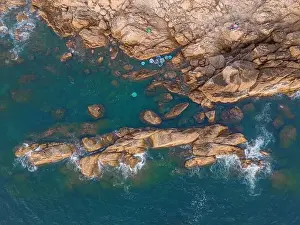 Aerial drone top view of beautiful waves crashing on the rocky island coast