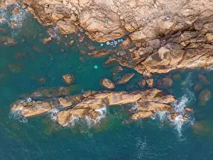 Aerial drone top view of beautiful waves crashing on the rocky island coast