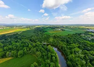 Aerial drone view over creek during daytime with trees in few and harsh sunlight