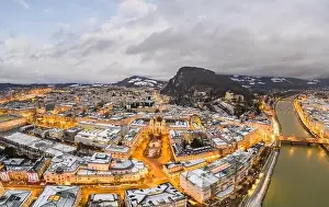 City Light Prints: Aerial drone view of Holy Trinity Church in Salzburg covered with snow in winter at dusk with city lights