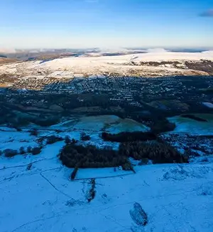 Aerial drone view of snow covered mountains and towns rising above the south east valleys, Wales