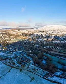 Aerial drone view of snow covered mountains and towns rising above the south east valleys, Wales