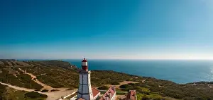 Aerial; drone view of white-red lighthouse Cabo Espichel on the edge of the earth; turquoise water of Atlantic ocean