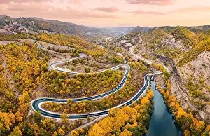 Aerial panoramic view of Venetikos river and serpentine highway road in autumn forest in Balkan Greece