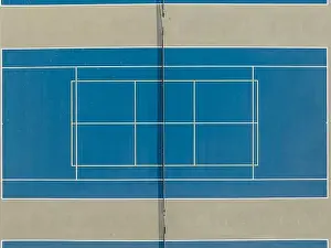 Aerial photo of outdoor blue tennis courts with yellow pickleball lines and gray out of bounds area
