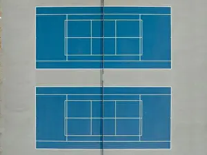 Aerial photo of outdoor blue tennis courts with yellow pickleball lines and gray out of bounds area