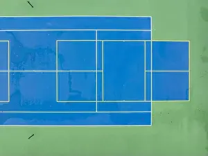 Aerial photo of unusually painted outdoor blue tennis courts with yellow pickleball lines and green out of bounds area