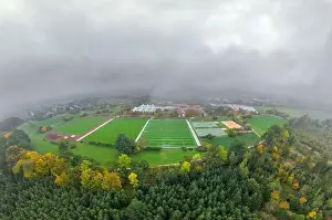 Foggy Landscape Prints: Aerial of a soccer pitch in the fall season with a lot of fog and a forest in the foreground