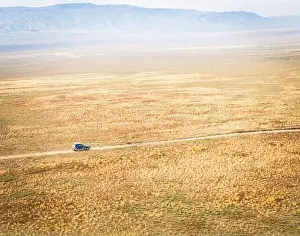 Blank Space Prints: Aerial view of 4WD automobile driving across deserted vast landscape and mountains background VAshlovani national park