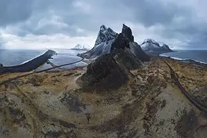 Eystrahorn Prints: Aerial view of asphalt road going between snowy mountain and blue ocean under cloudy sky in Eystrahorn