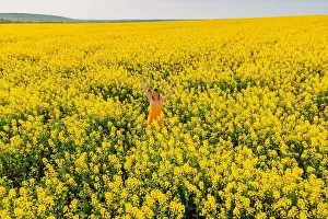 Aerial view of attractive woman at blooming rapeseed field. Yellow flowers and happy woman