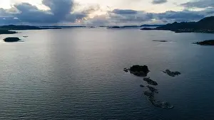 Placid Prints: Aerial view of a calm fjord with small rocky islands and distant mountains under a cloudy sky